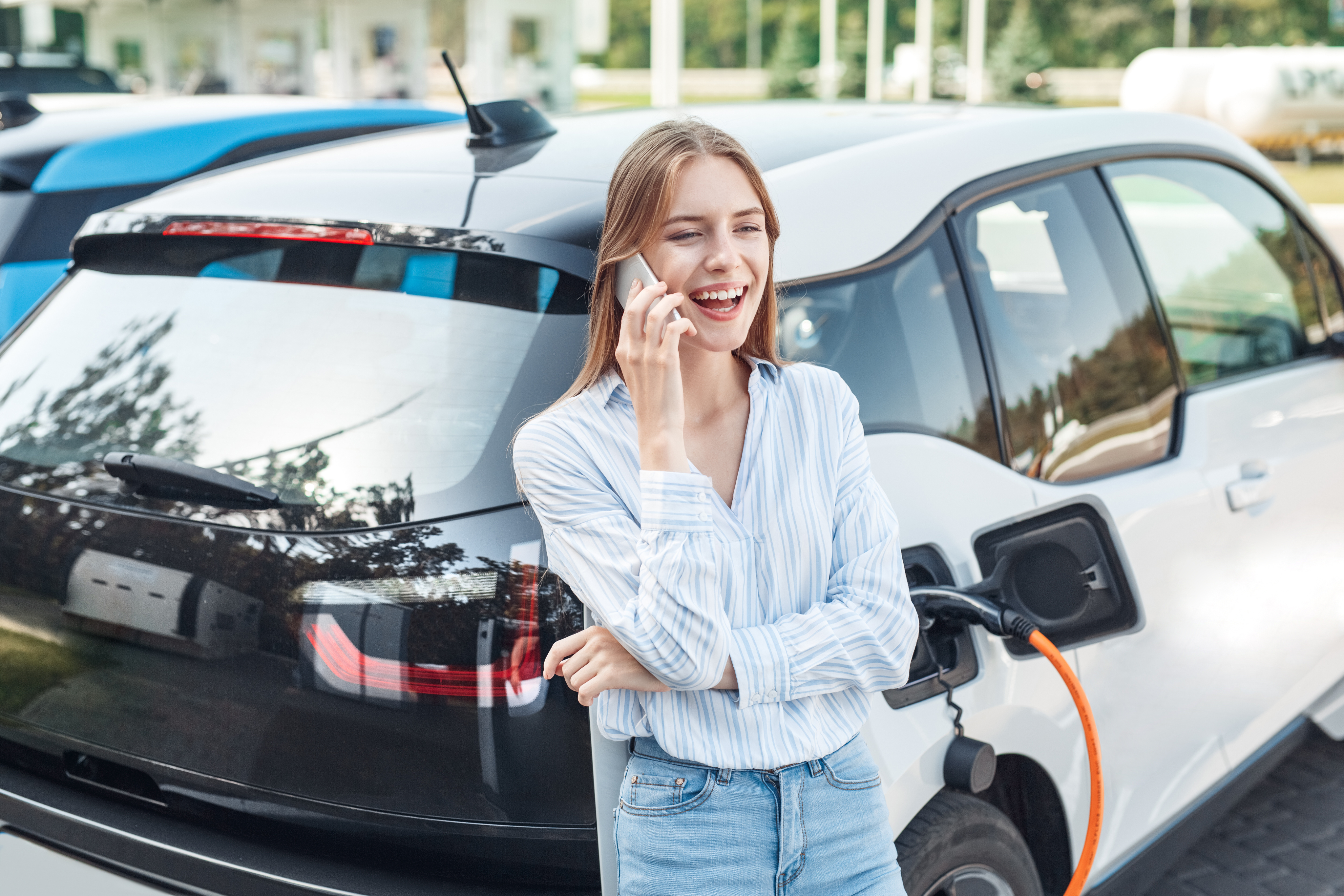 Woman on phone leaning on electric vehicle